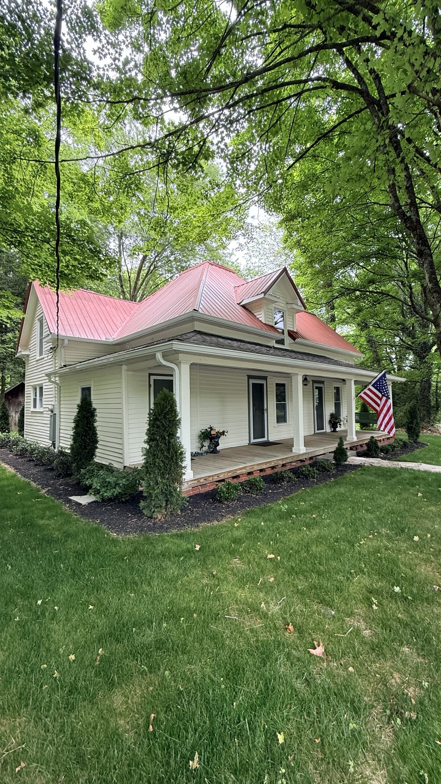 A white home with a red roof and covered porch surrounded by trees